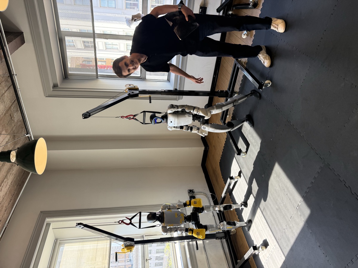 Two humanoid robots on gantry frames in a robotics lab