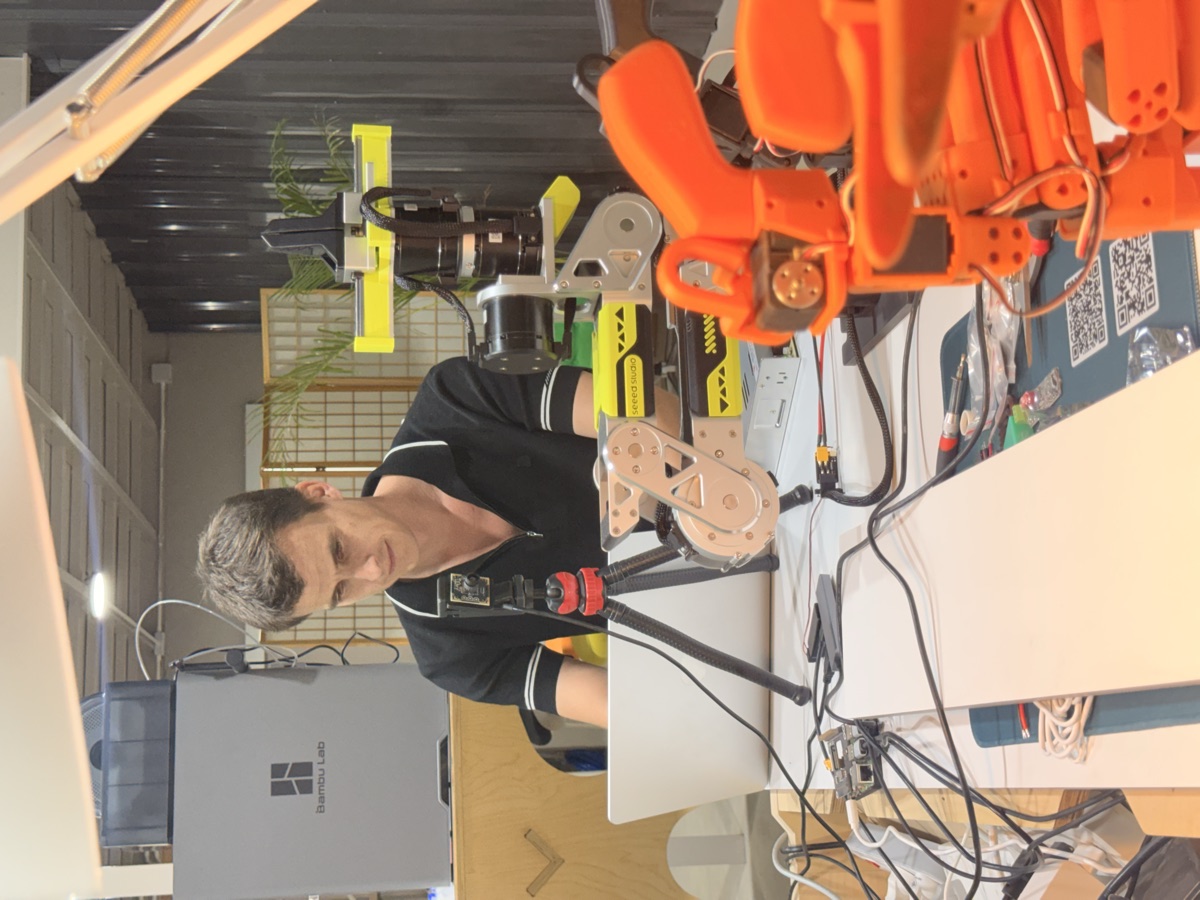 Working at a laptop beside a robot arm and a 3D printer