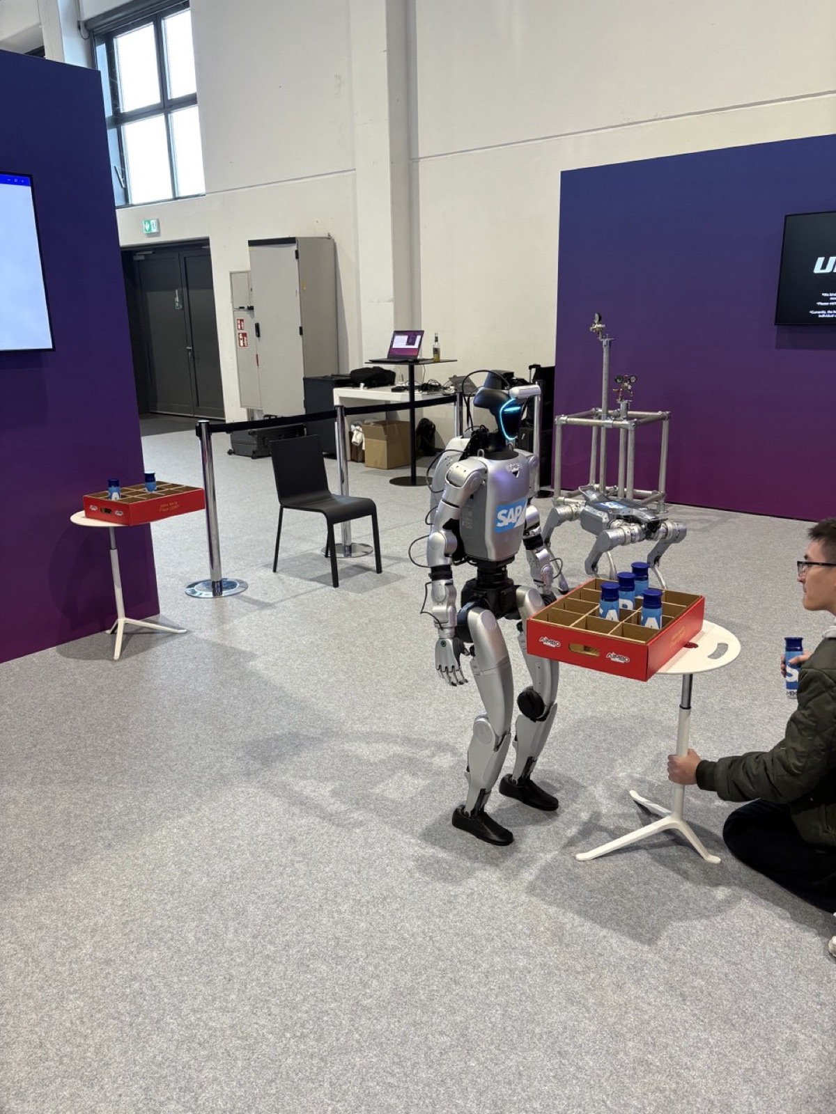 An SAP-branded humanoid robot carrying a crate of drinks at a conference